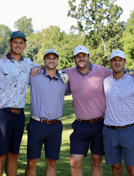Four men posing for a photo on a golf course with trees in the background