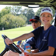 Two people in a golf cart on a golf course with trees in the background