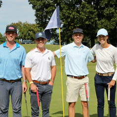 Group of six people on a golf course posing for a photo with a flag in the background.