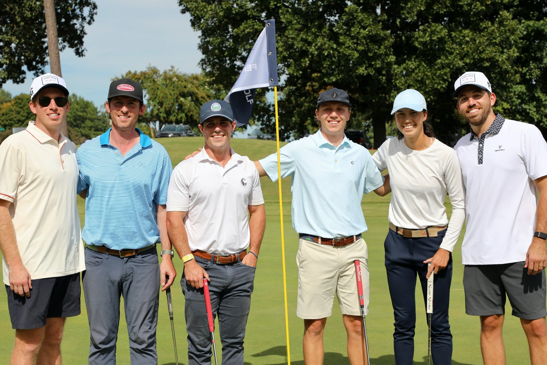 Group of six people on a golf course posing for a photo with a flag in the background.