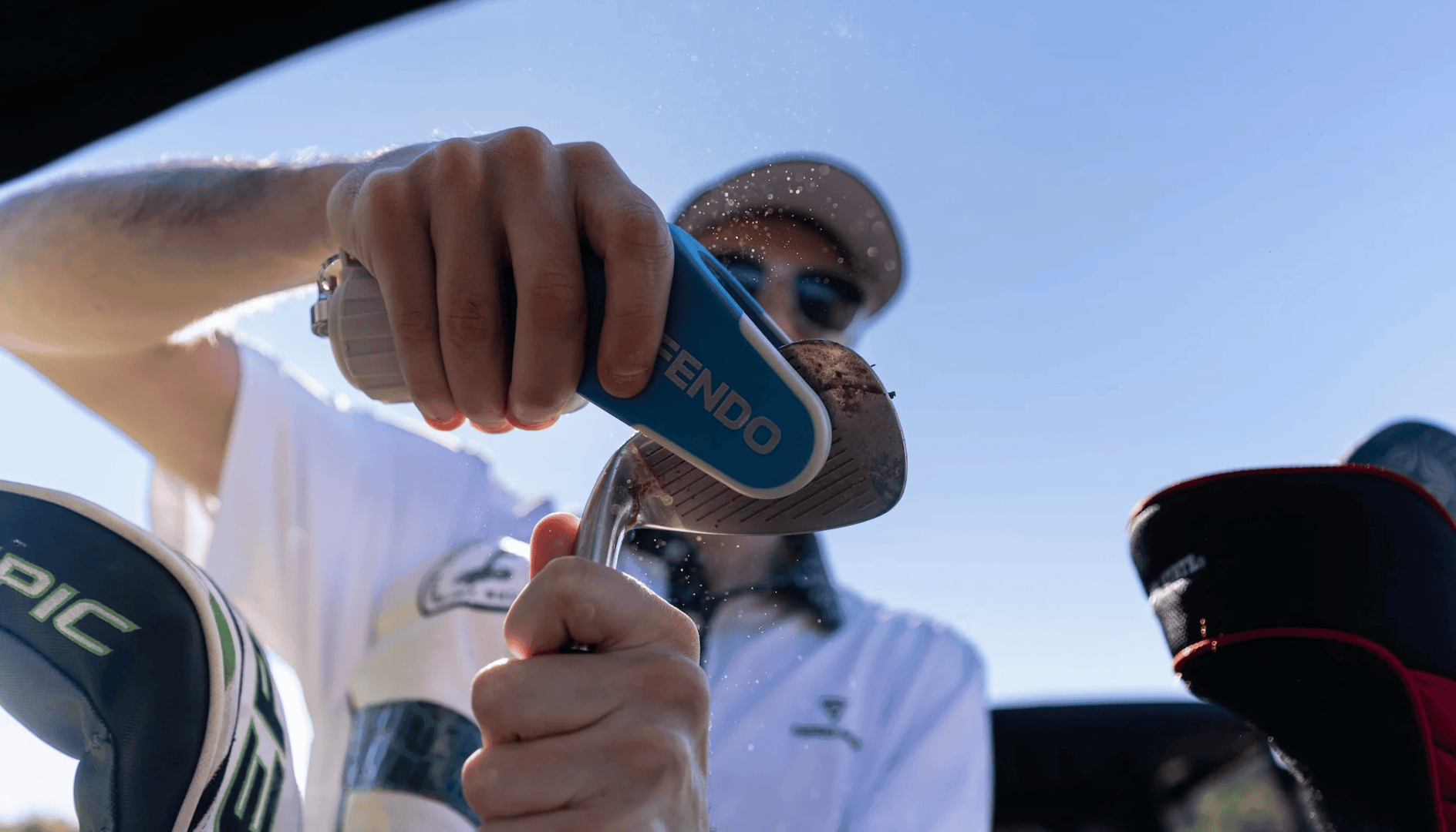 Person using a Fendo to clean his golf wedge with a clear sky background