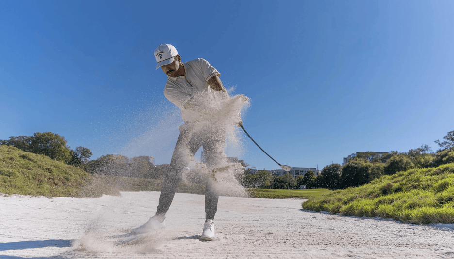 Person hitting a bunker shot on a sunny day with trees in the background