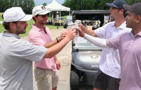 Four men toasting with drinks in a golf course setting