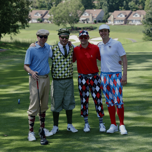 Four men posing for a photo on a golf course with colorful outfits.